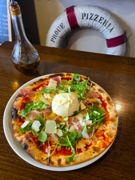 Pizza du moment garnie de burrata, jambon cru et roquette